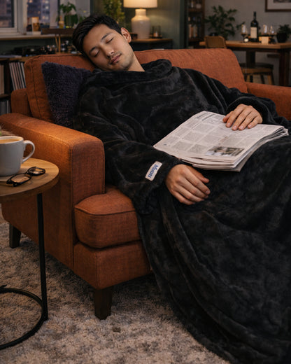 Man asleep in an armchair with a newspaper on his lap, wearing a Black Slanket