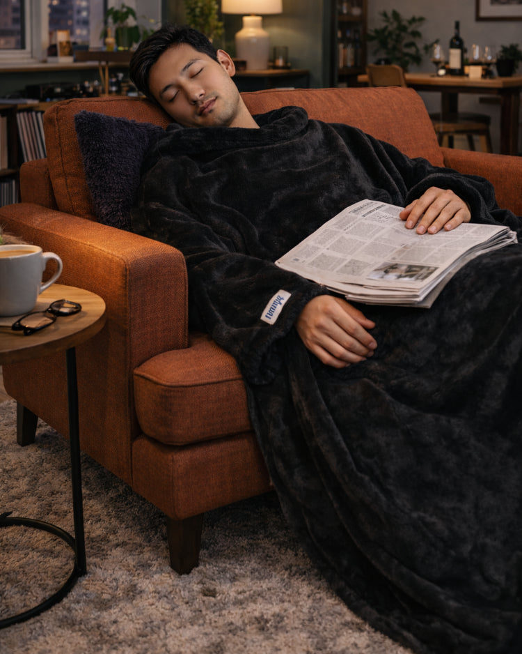 Man asleep in an armchair with a newspaper on his lap, wearing a Black Slanket