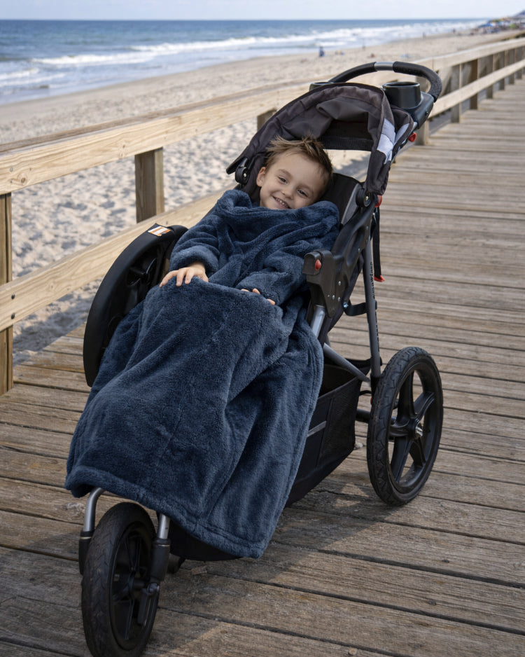 Product image of a little boy using Stroller Slanket while sitting in his stoller by the ocean