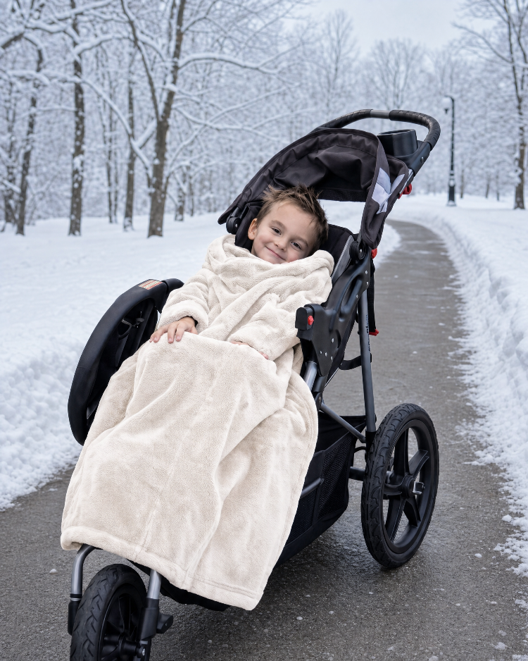 Boy in a stroller wrapped in a Cloud Dancer Stroller Slanket on a snowy path